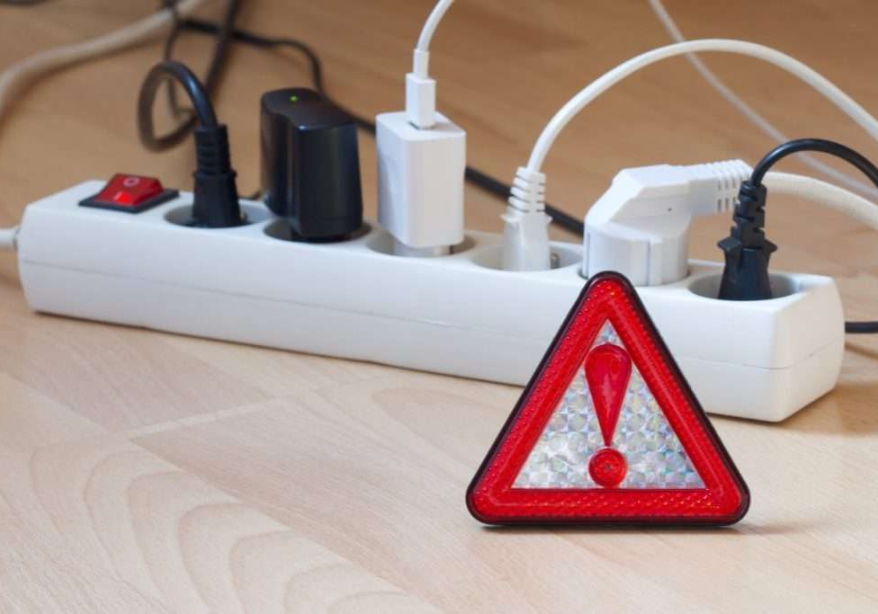 Electrical outlets with every device plugged into an outlet with a danger symbol indicating do not overload your circuits