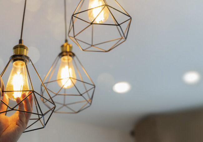 An electrician is installing spotlights on the ceiling choosing between energy save and cheap incandescent lamp while changing light in the 
