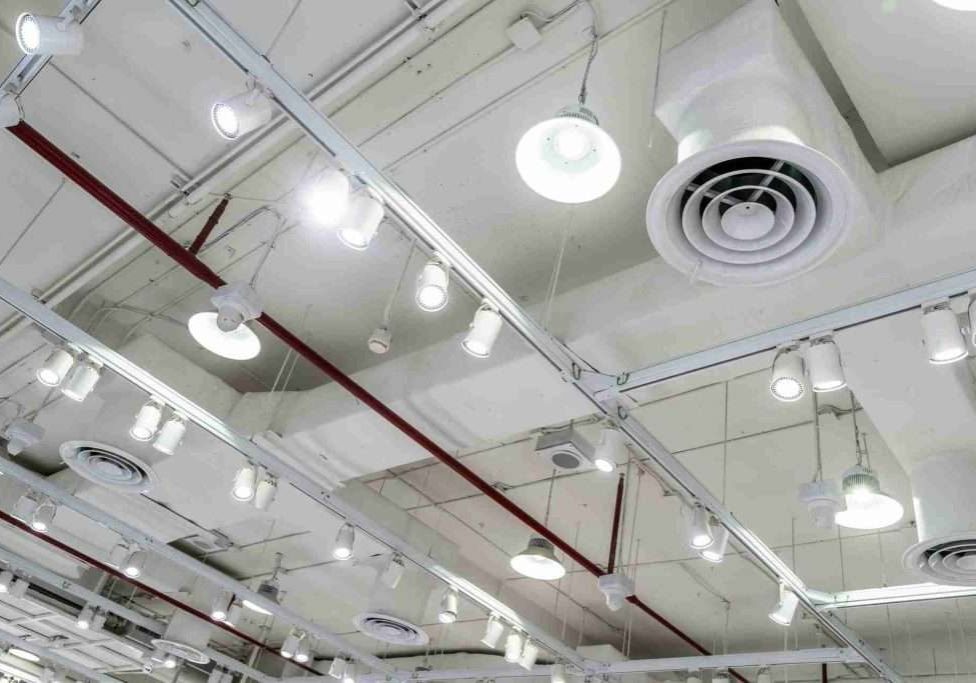 Bare ceiling with air duct, CCTV, air conditioner pipe and fire sprinkler system on white ceiling wall. Air flow and ventilation system. Ceiling lamp light with opened light. Interior architecture.